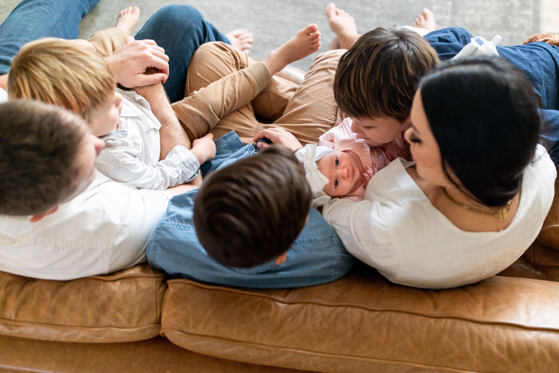 Family Photographer, a mother, father, and young kids cuddle on the couch together as they welcome a newborn baby